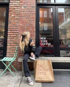 a woman sitting on a bench next to a big brown bag and a new york coffee sign