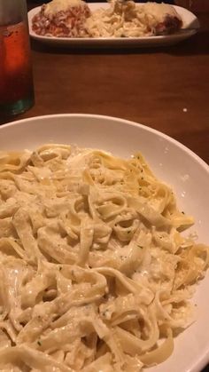 a white plate topped with pasta and sauce next to a glass of soda on a table