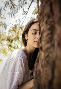 a woman leaning against a tree with her eyes closed