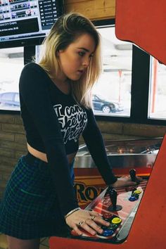 a woman standing in front of a pinball machine with her hands on the board