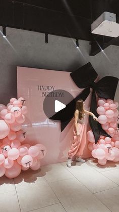 a woman standing in front of a display with pink balloons and black bows on it