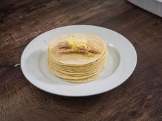 a stack of corn tortillas on a white plate with shredded cheese and butter