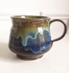 a brown and blue coffee cup sitting on top of a counter next to a white wall