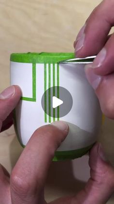 two hands holding a green and white cup with a video playing button on the side