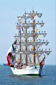 a large white ship with lots of flags on it's sails in the ocean