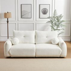 a white couch sitting on top of a hard wood floor next to a wall with pictures