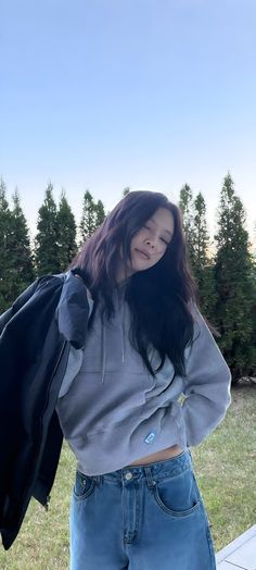 a woman standing in front of some trees with her jacket over her shoulder and looking at the camera