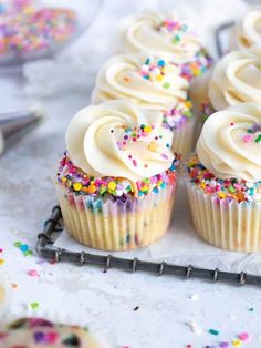 several cupcakes with white frosting and sprinkles on a tray