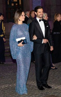 a man in a tuxedo walking next to a woman in a blue dress