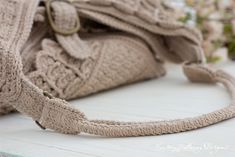 a beige purse sitting on top of a white table next to some pink flowers and greenery