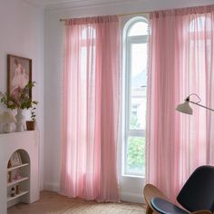 a living room with pink curtains and a chair in front of a window that is open