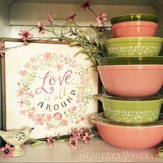 pink and green bowls stacked on top of each other in front of a framed love is around sign