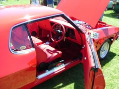 the interior of an old red car with its door open and people standing around looking at it