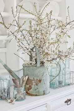 an old watering can with flowers in it on top of a mantle next to glass jars