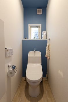 a white toilet sitting inside of a bathroom next to a blue wall and wooden floor