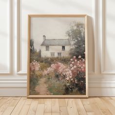 an oil painting of a house and flowers in front of a white wall with wooden flooring