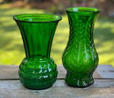 two green glass vases sitting on top of a wooden table next to each other