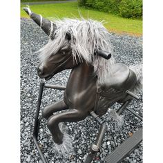 a black rocking horse with white manes on it's head and legs sitting in gravel