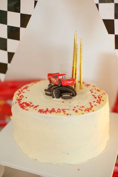 a white cake with red and yellow frosting on top, decorated with cars in the middle