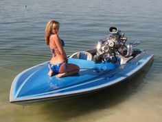 a woman sitting on the back of a blue and silver boat with a jet ski attached to it