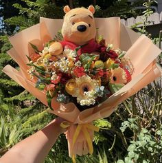 a person holding a bouquet of flowers with a teddy bear in the middle and trees behind them