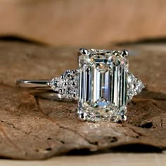 an emerald - cut diamond ring sits on top of a leaf