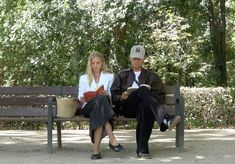 two people sitting on a bench in the park, one reading a book and the other reading a book