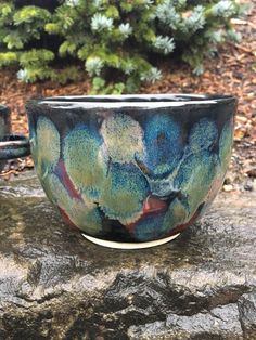 a blue and green bowl sitting on top of a rock