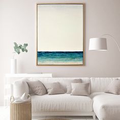 a living room with a white couch and blue ocean painting on the wall above it