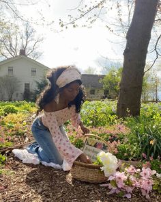 a woman kneeling down next to a basket filled with flowers in front of a tree