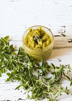 a small glass bowl filled with green pestle next to fresh herbs on a white wooden surface