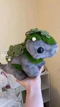 a person holding a stuffed animal with green leaves on it's head and eyes