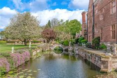 a river running through a lush green park next to tall brick buildings on either side