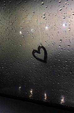 rain drops on the window with a heart shaped sticker hanging from it's side