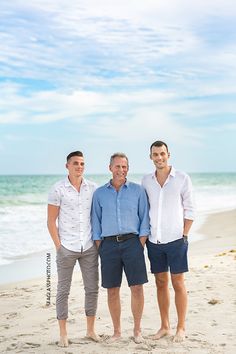 three men standing next to each other on the beach in front of an ocean and sky