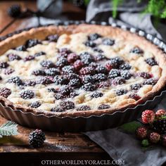 a pie with berries on it sitting on top of a wooden table next to some blackberries