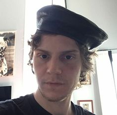 a young man wearing a black hat and looking at the camera while standing in front of a mirror