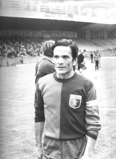 a black and white photo of a man standing in front of a soccer field with people watching