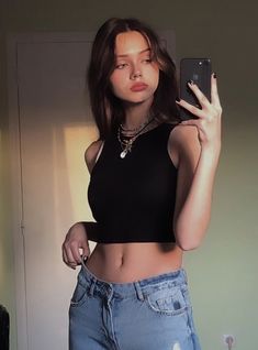 a young woman taking a selfie with her cell phone in the mirror while wearing high waist jeans