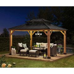 an outdoor gazebo lit up at night with lights on the patio and furniture around it