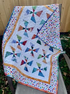 a colorful quilt on a chair in the grass next to a wooden fence and tree