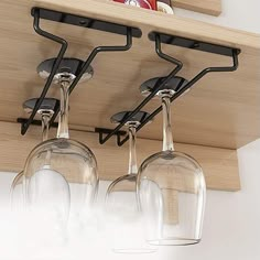 three wine glasses are hanging from the ceiling in front of a wooden shelf with hooks