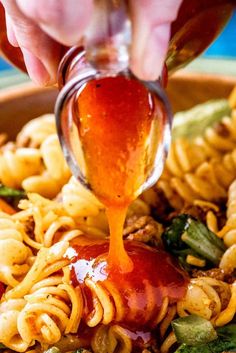 someone pouring sauce over some noodles in a bowl