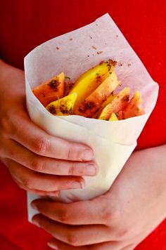 a woman holding a paper bag filled with bananas and other food items in her hands