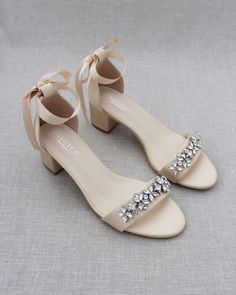 a pair of white shoes with bows and jeweled buckles on the toes, sitting on a gray surface