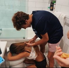 three people are in the bathroom and one person is brushing her hair while another woman sits on the toilet