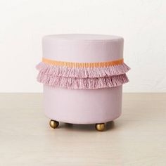 a pink stool with tassels on it sitting on top of a wooden table