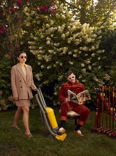 two people dressed as clowns are sitting in the grass and one person is reading a magazine