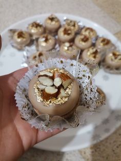 a hand holding a chocolate dessert with nuts in it on top of a white plate