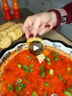 a person dipping sauce on top of a pizza with green onions and cheese crackers